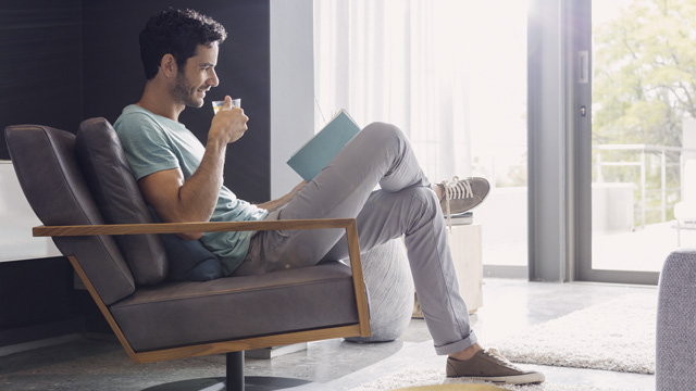 Man sitting in armchair drinking coffee reading