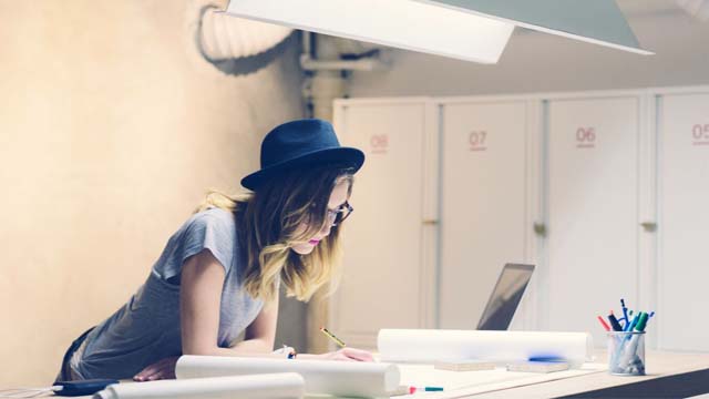 Woman in hat leaning over desk with paper 