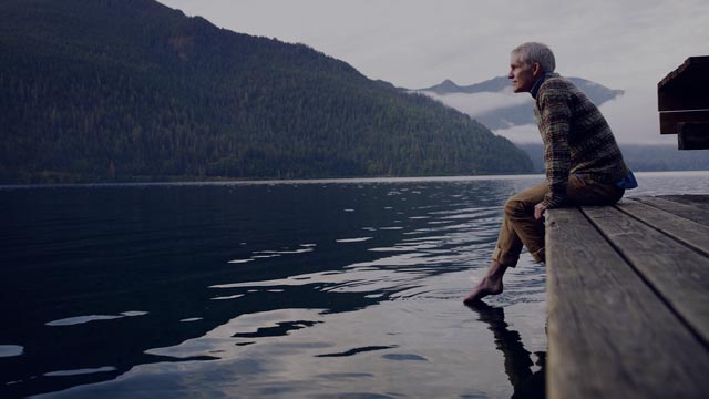 Ældre mand på bro, der kigger ud over en sø