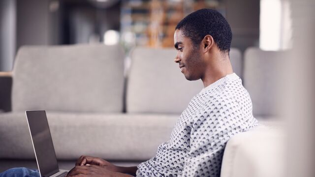Young man sitting at sofa looking at laptop - small
